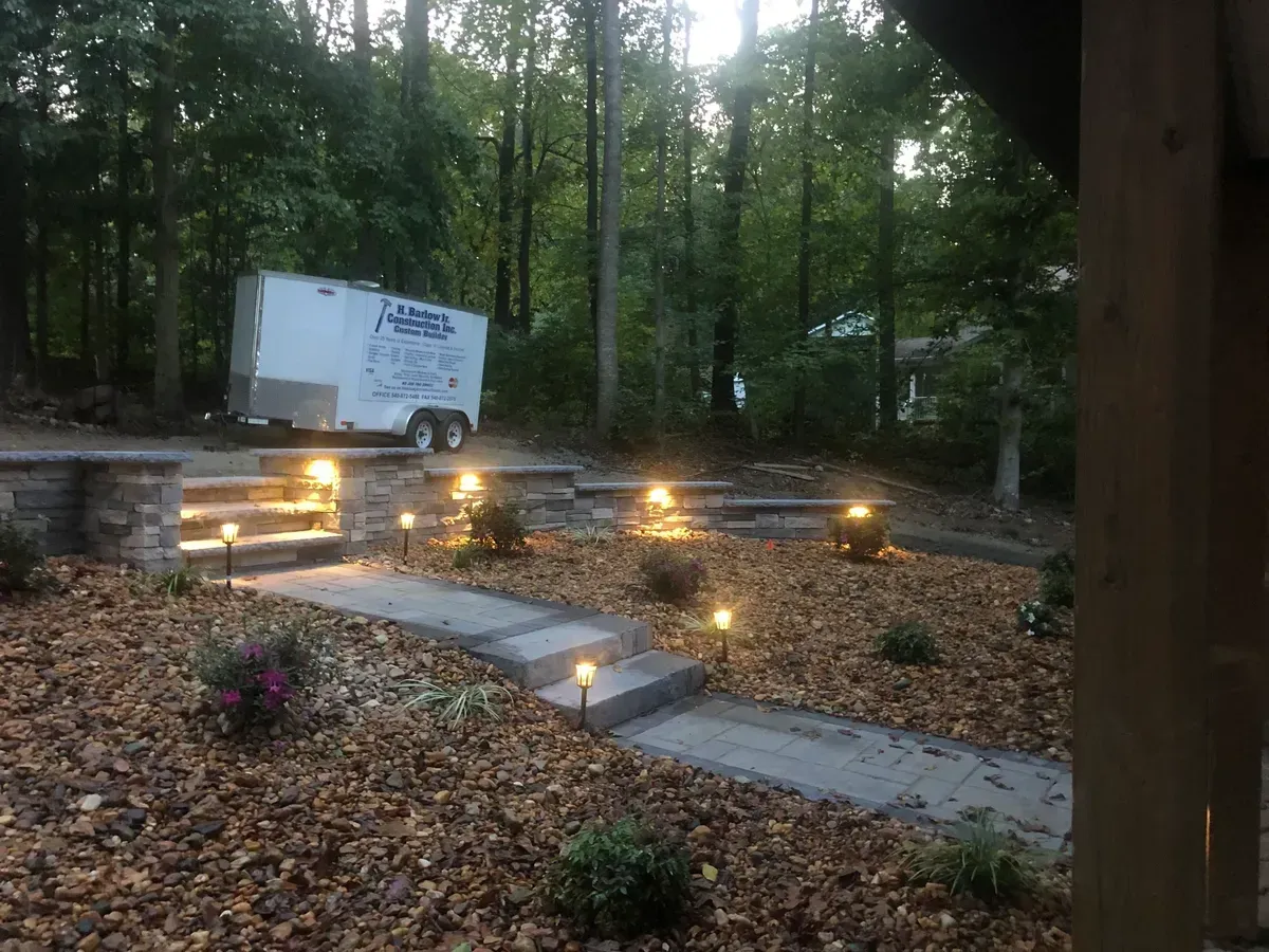 Wooded outdoor patio with stone steps, glowing pathway lights, and fallen leaves.