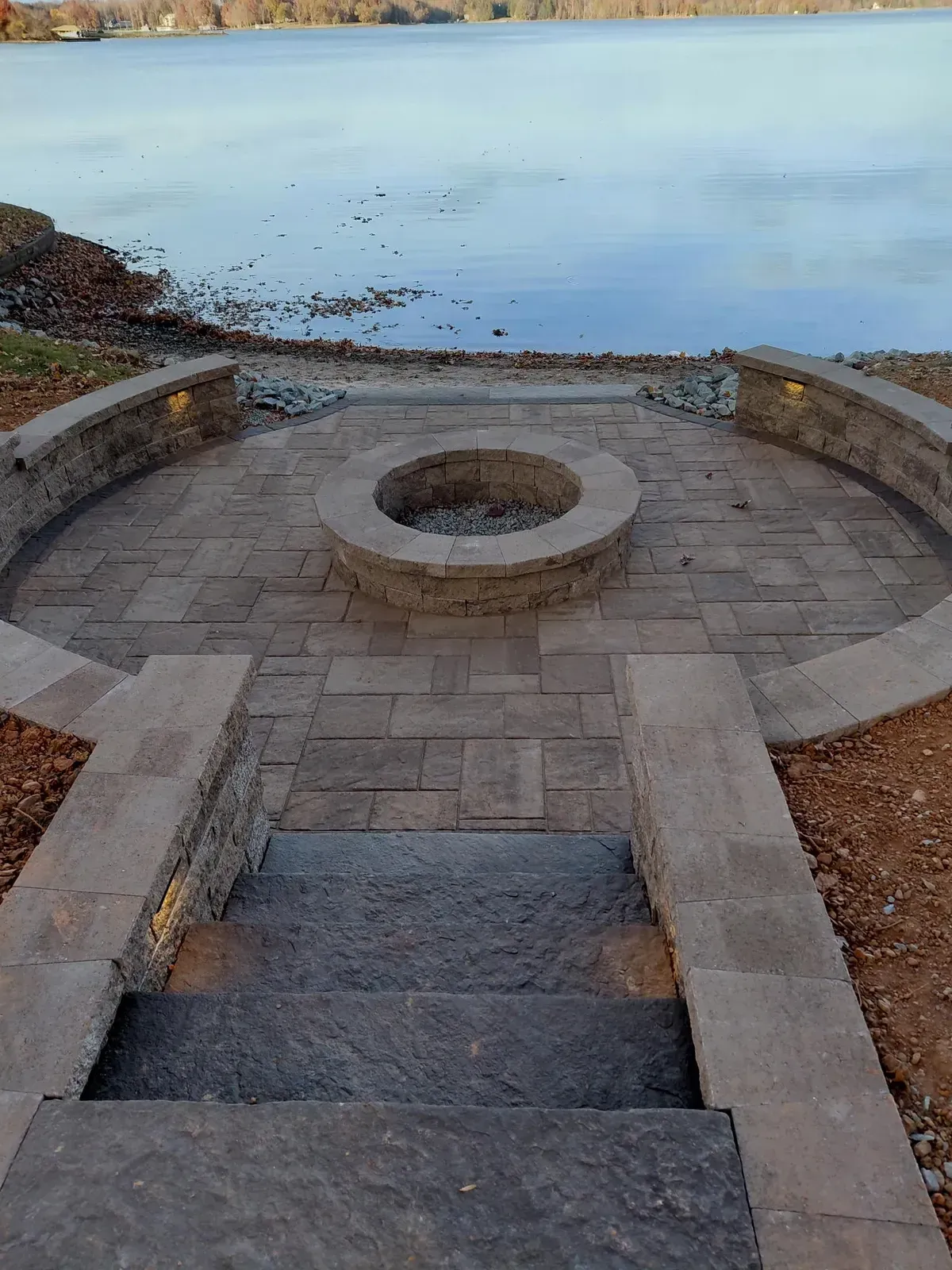 Stone steps lead to a paved lakeside fire pit with calm water beyond.