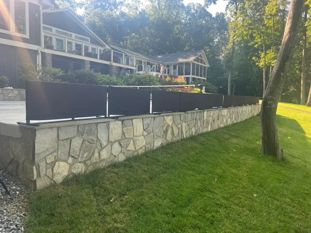 Stone retaining wall beside a grassy slope, with houses and trees in the background