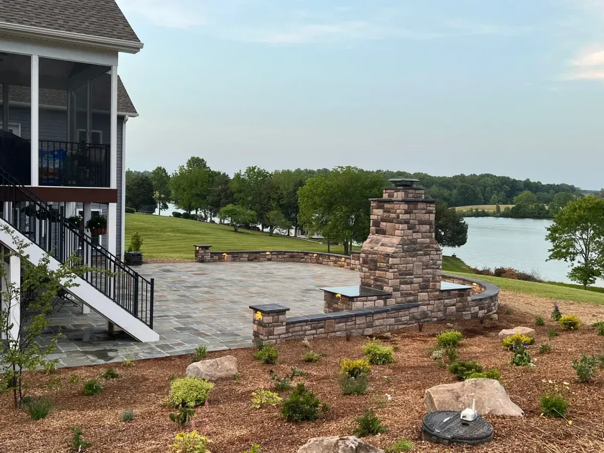 Lakeside patio with stone fire pit, landscaped rocks, and a house deck overlooking the water