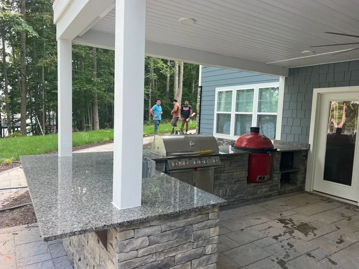 Covered outdoor kitchen with granite counters, grill, red smoker, and nearby people in the background.