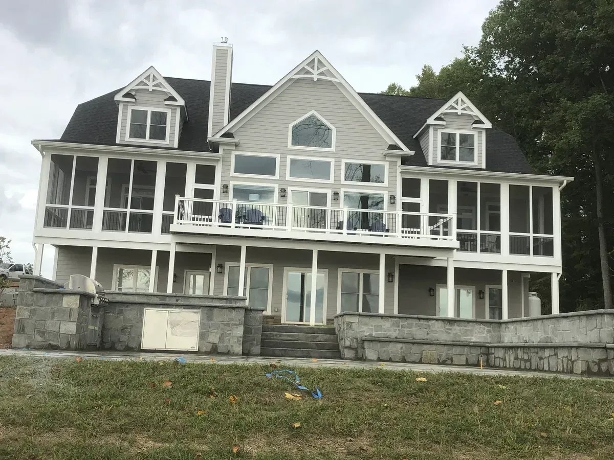 Large gray house with white trim and wraparound porch on a grassy hillside