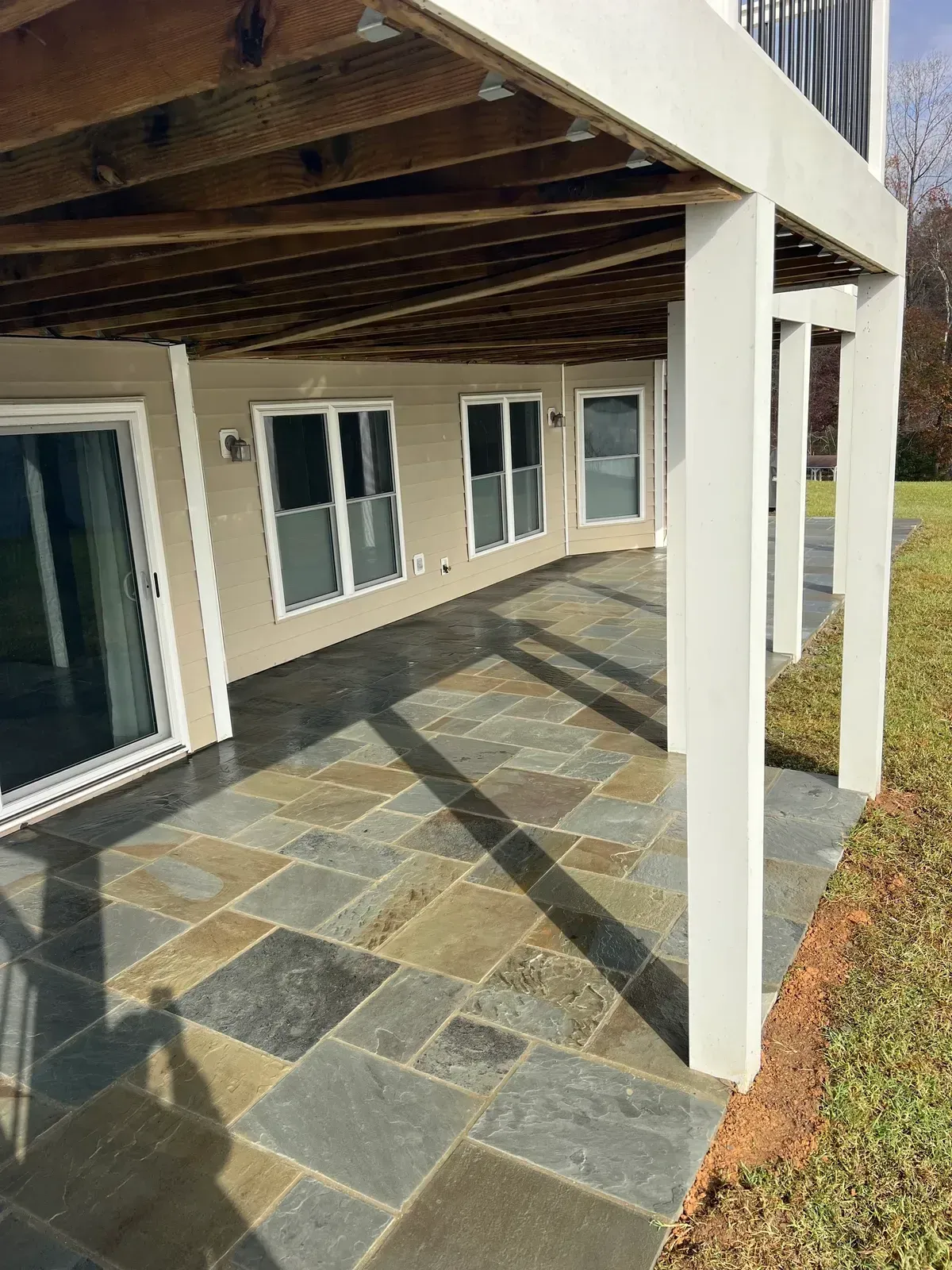 Covered porch with stone tile floor, white columns, and sliding glass doors on a beige house.