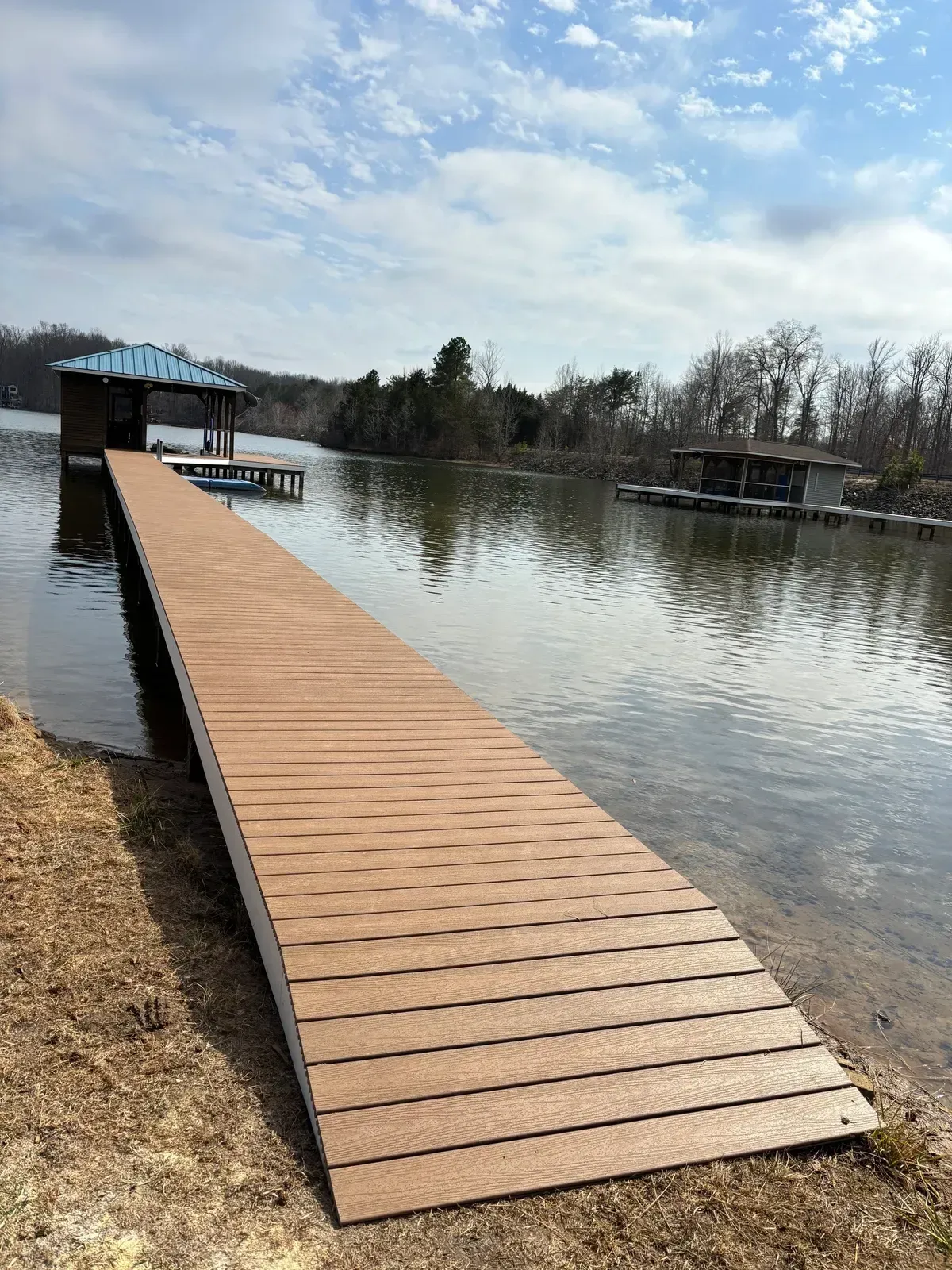Wooden dock extending into a calm lake under a cloudy sky, with shoreline trees in the distance