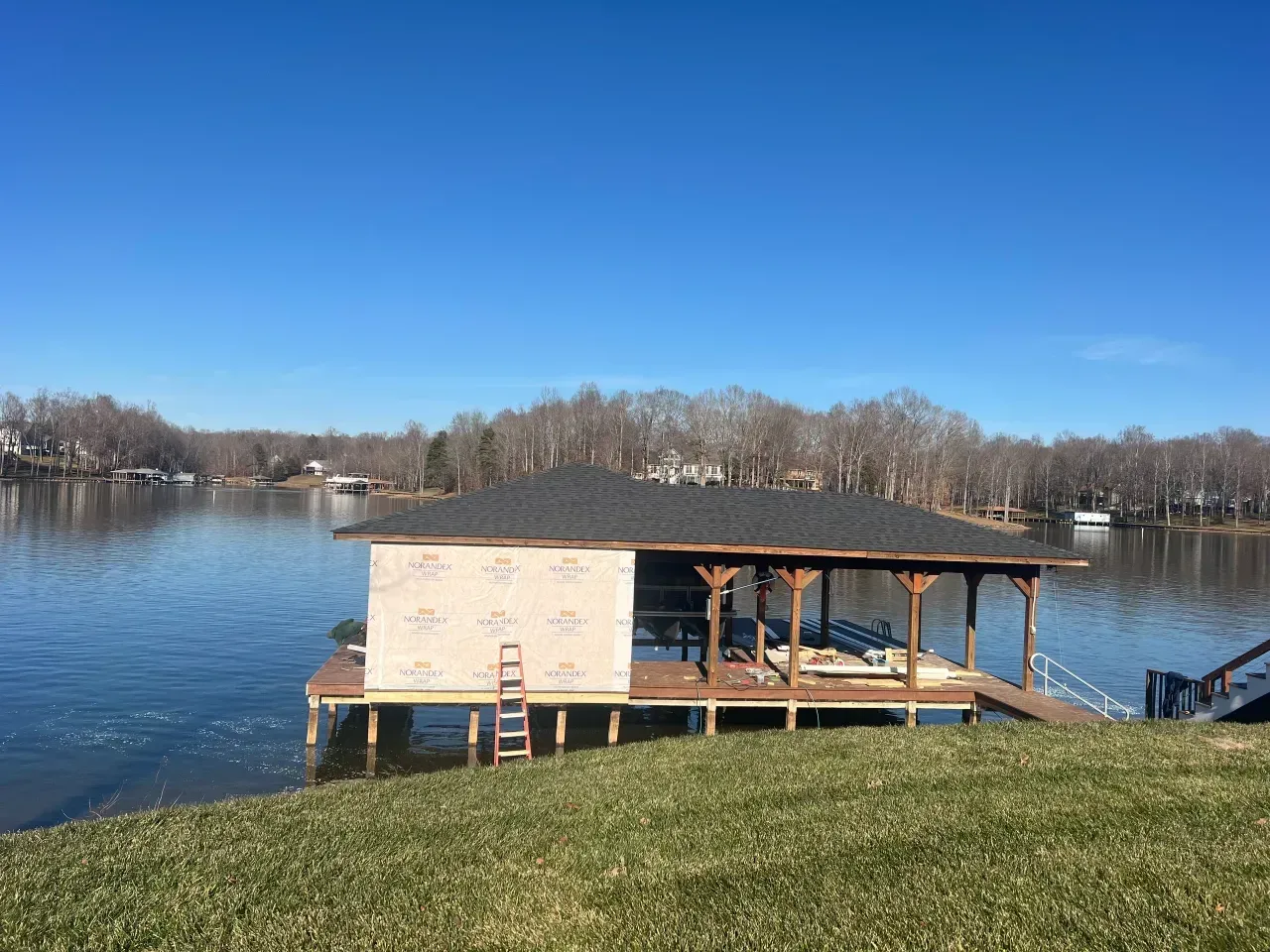 Wooden lakeside gazebo on a grassy shore under a clear blue sky