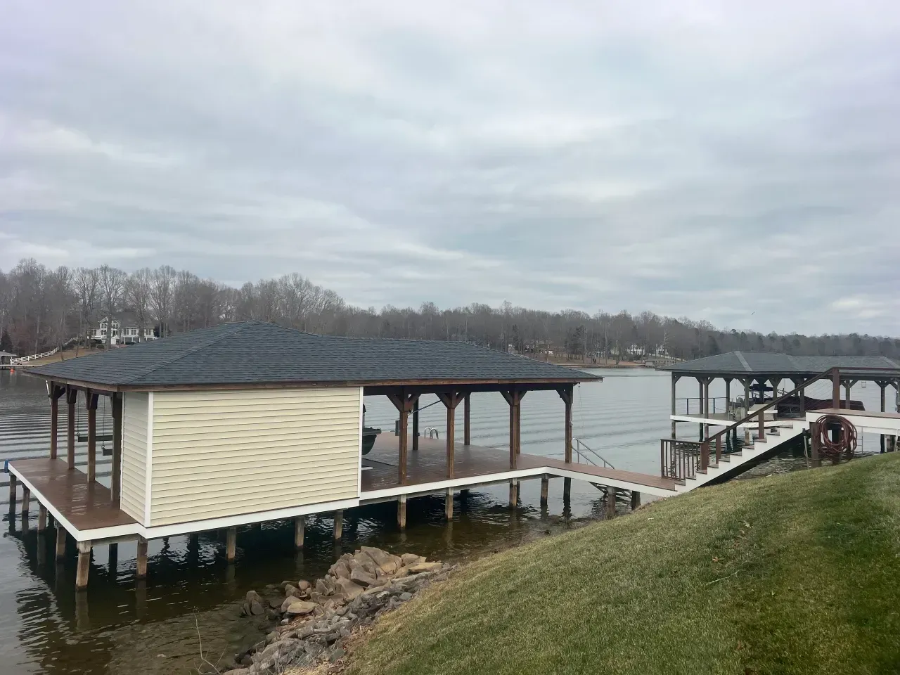 Covered dock on calm water beside a grassy shoreline under a cloudy sky