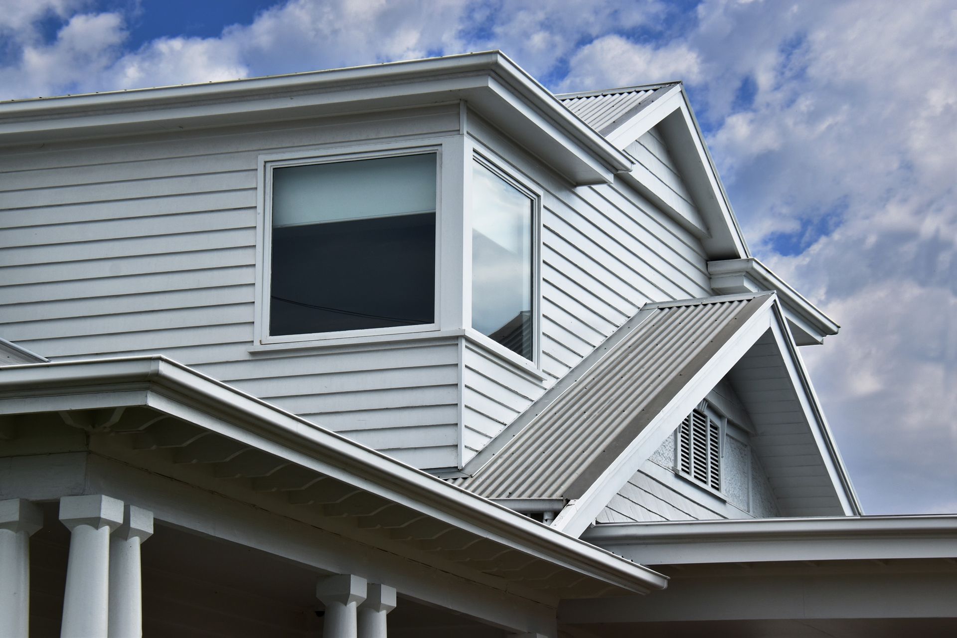White house exterior with siding, a bay window, and a sloped roof against a cloudy sky.