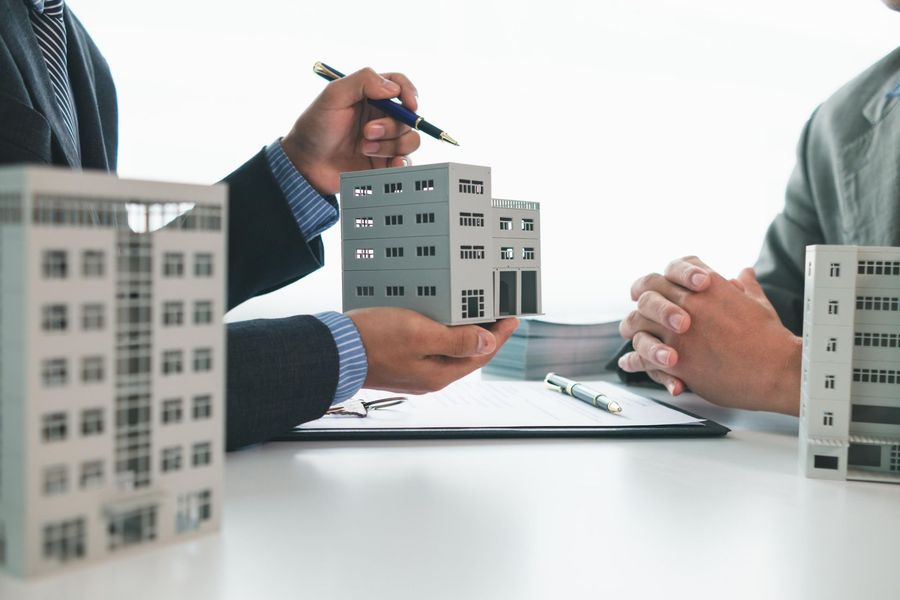 Man in suit points to building model; another man listens. 