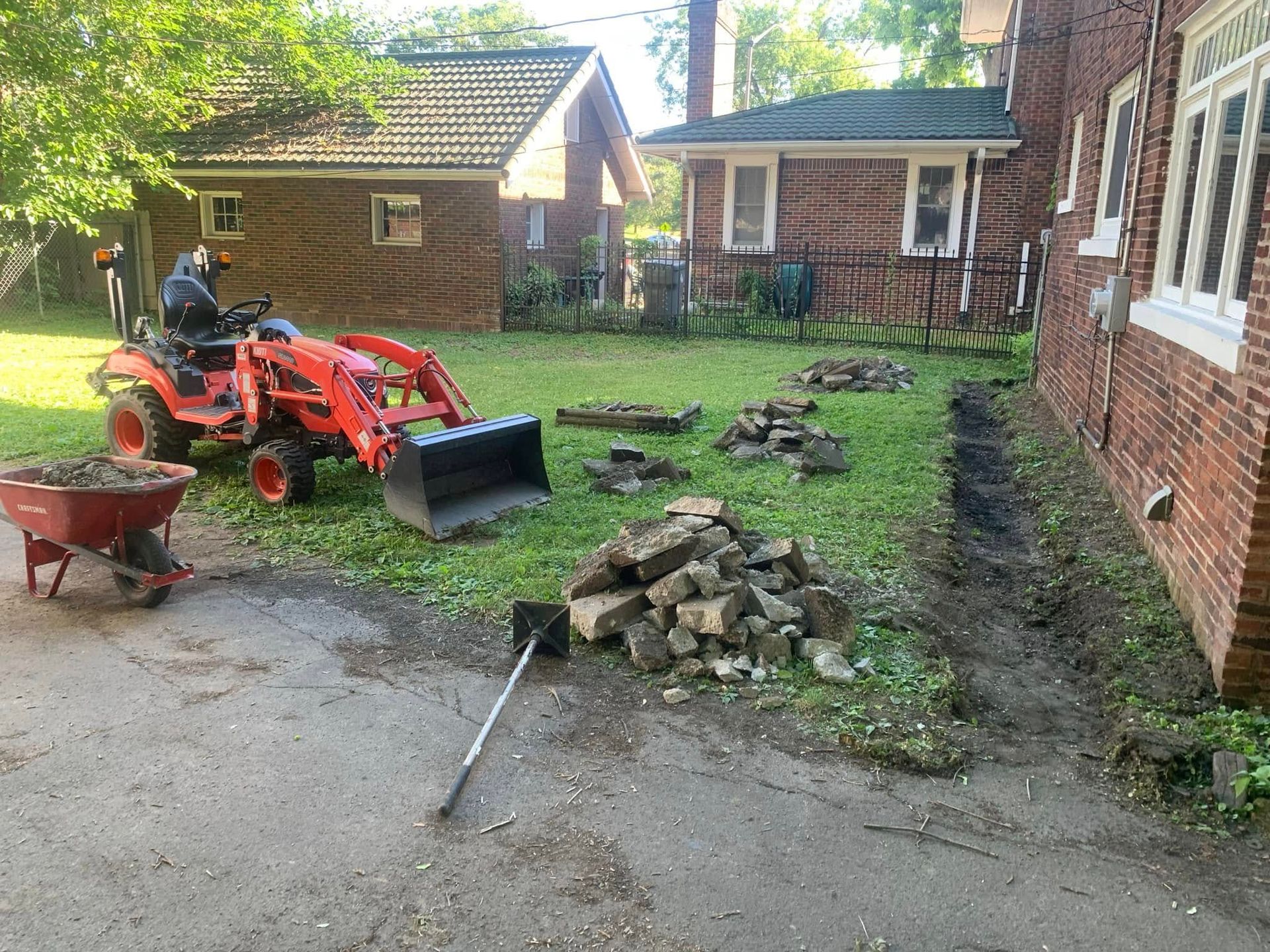 Backyard with orange tractor, wheelbarrow, fire pit stones, and brick house