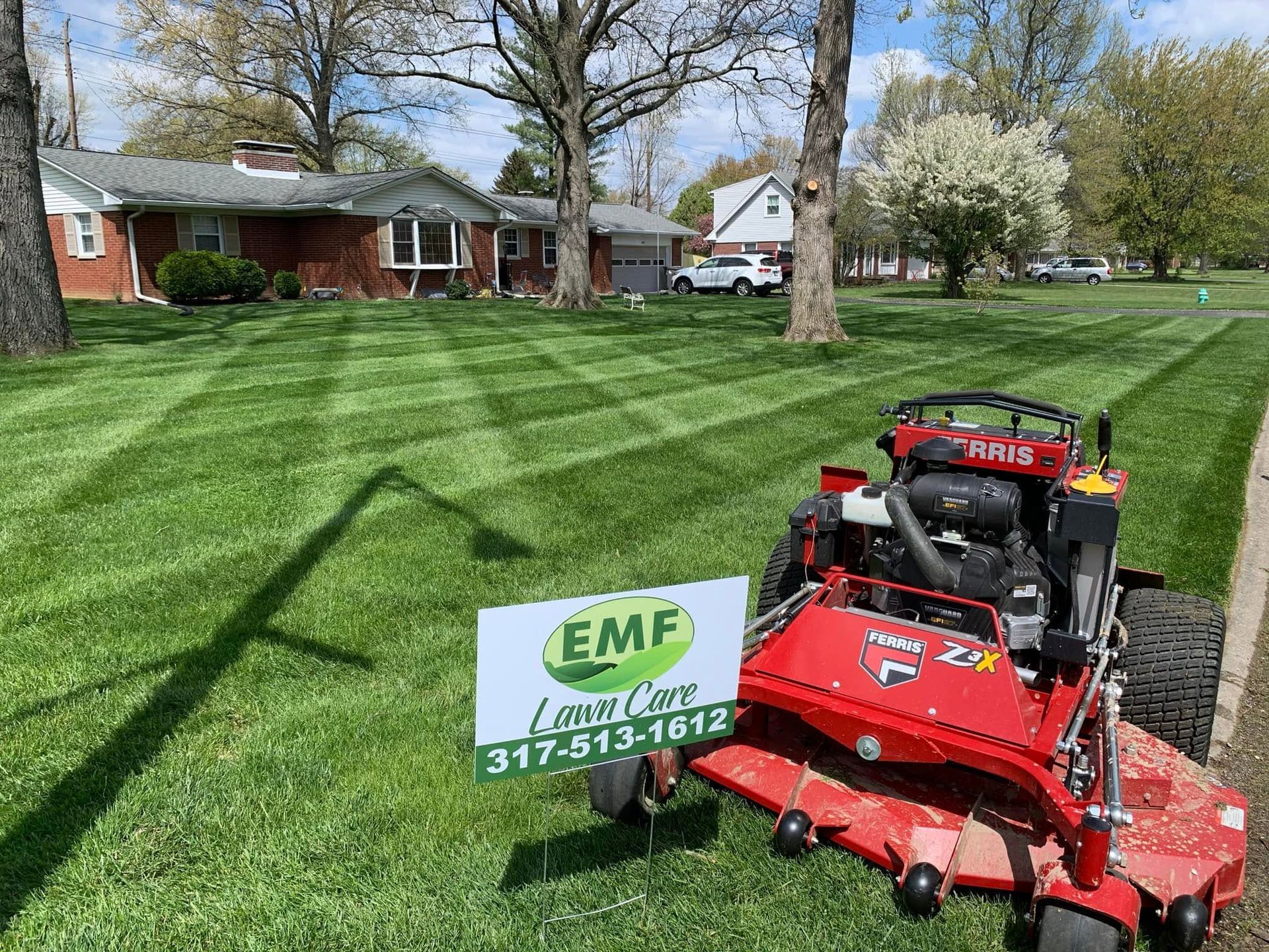 Red lawn mower on striped green lawn beside a house and EWD Lawn Care sign