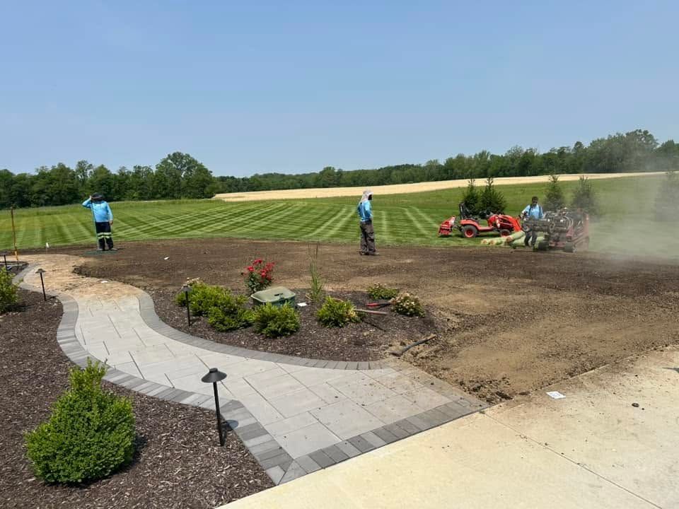 Garden workers edging a curved flower bed beside a paved path on a sunny day
