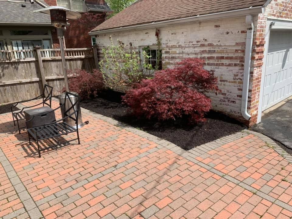 Brick patio with outdoor table and chairs beside a house and red shrubbery