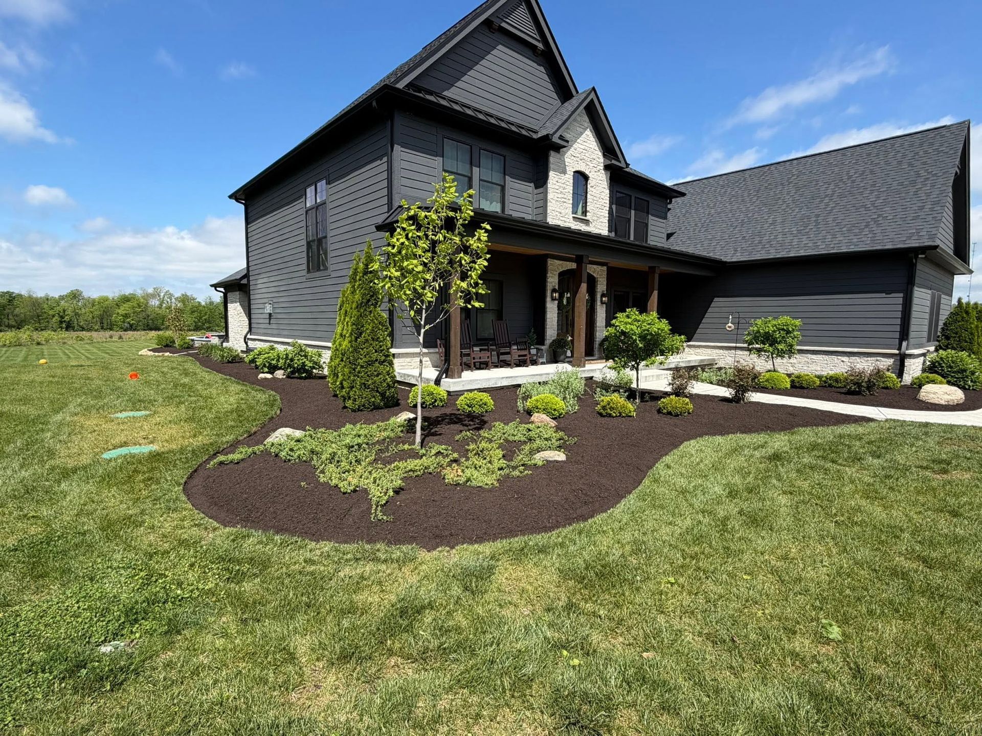 Dark gray house with a gabled roof and landscaped front yard under a blue sky