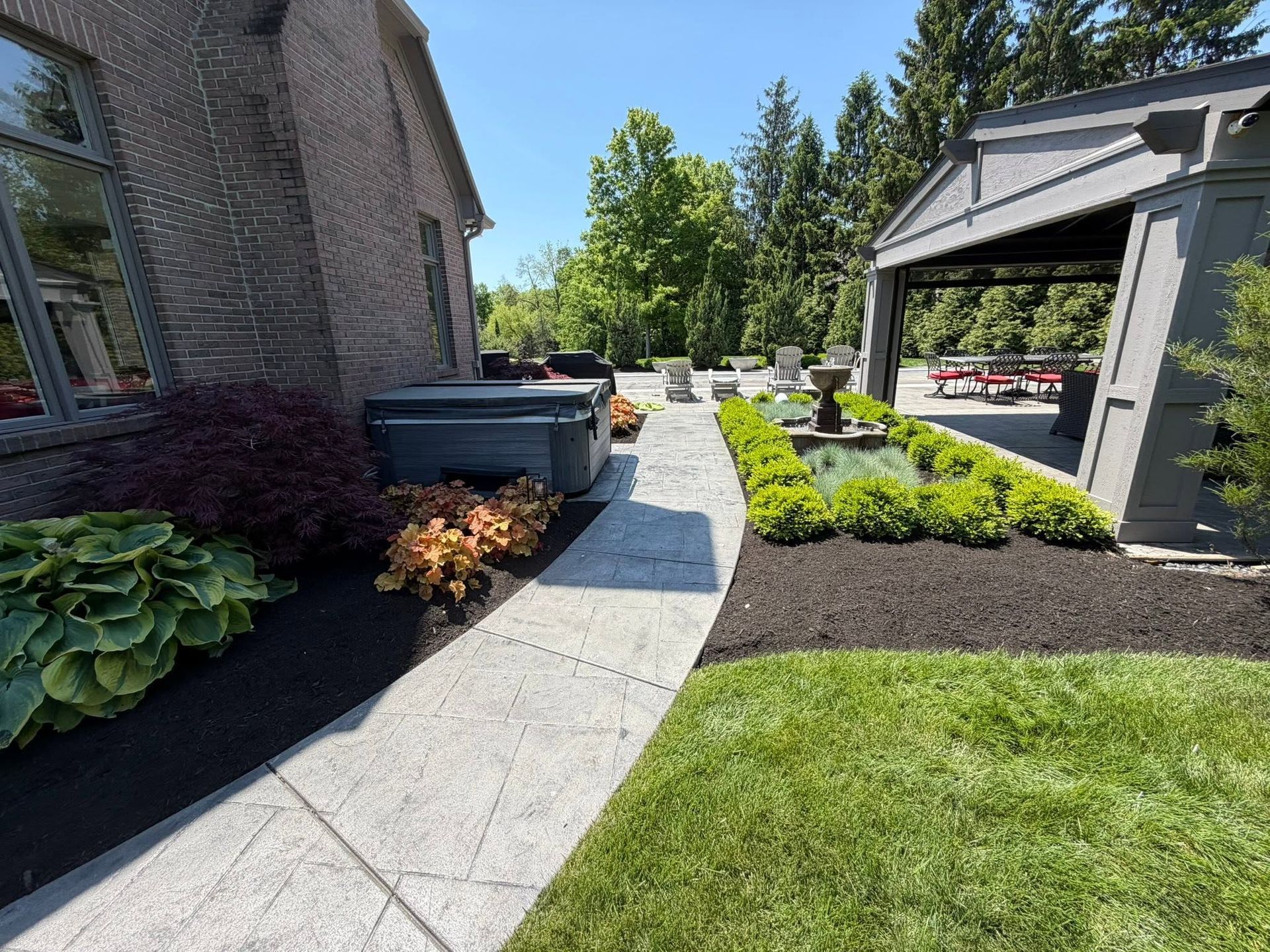 Curved stone walkway beside a brick house, landscaped with shrubs and mulch under a sunny blue sky