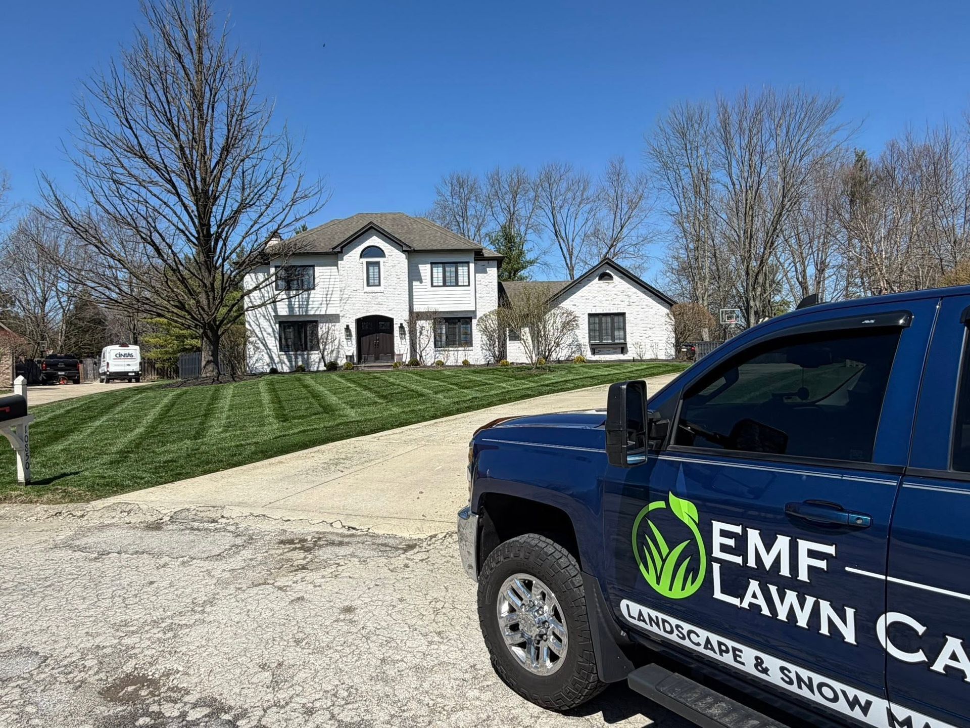 Suburban home with gravel driveway; blue EMF Lawn Care truck parked in the foreground.
