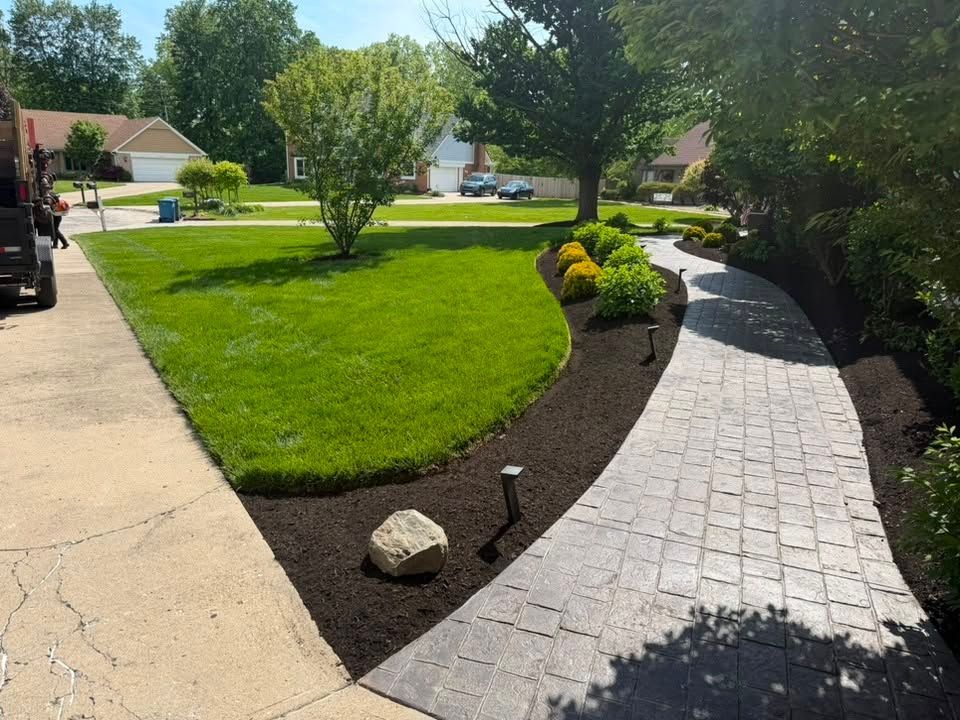 Curved gray paver walkway beside a green lawn and flower bed in a sunny suburban yard