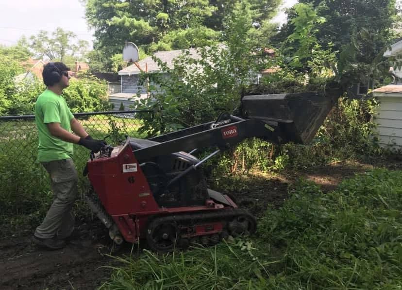 Worker operating a red wood chipper in a leafy backyard garden