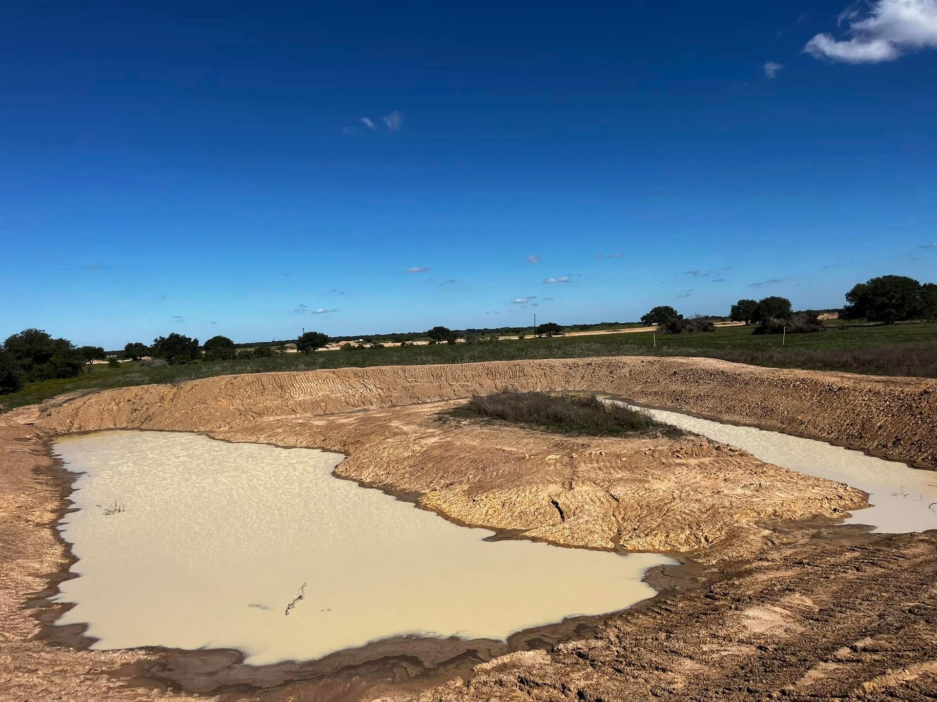 Partially filled ranch pond with island after pond construction in Texas