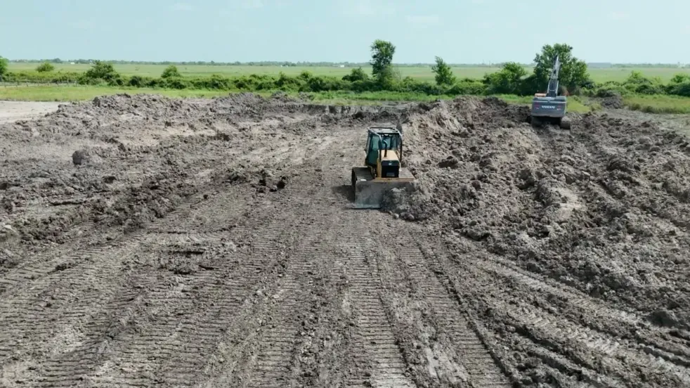 Skid steer and excavator working inside the developing pond excavation in Cat Spring, Texas