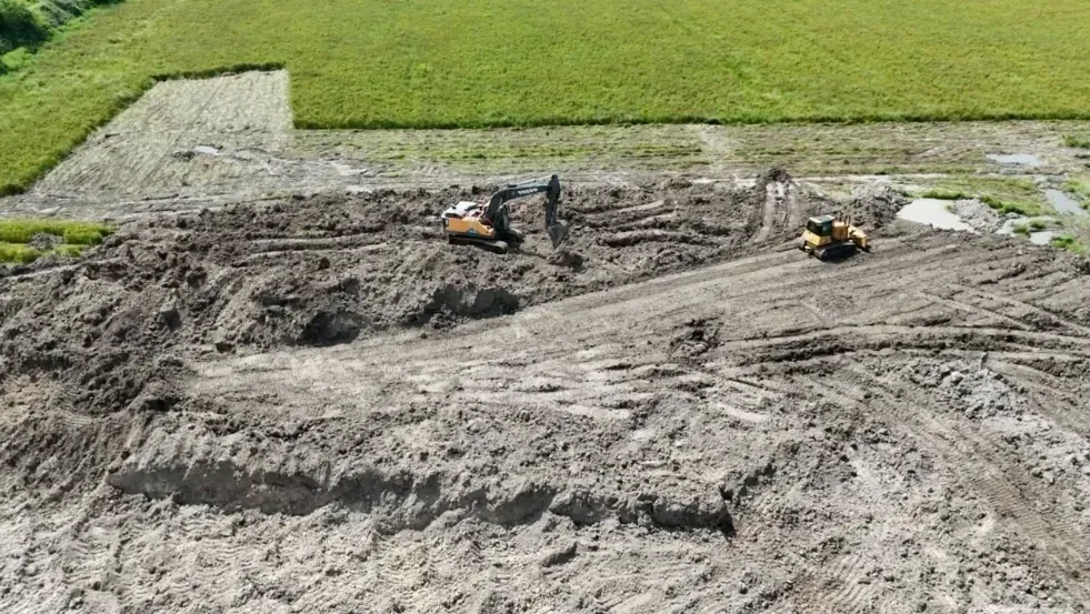 Excavator and dozer beginning the one-acre pond excavation on rural acreage in Cat Spring, Texas