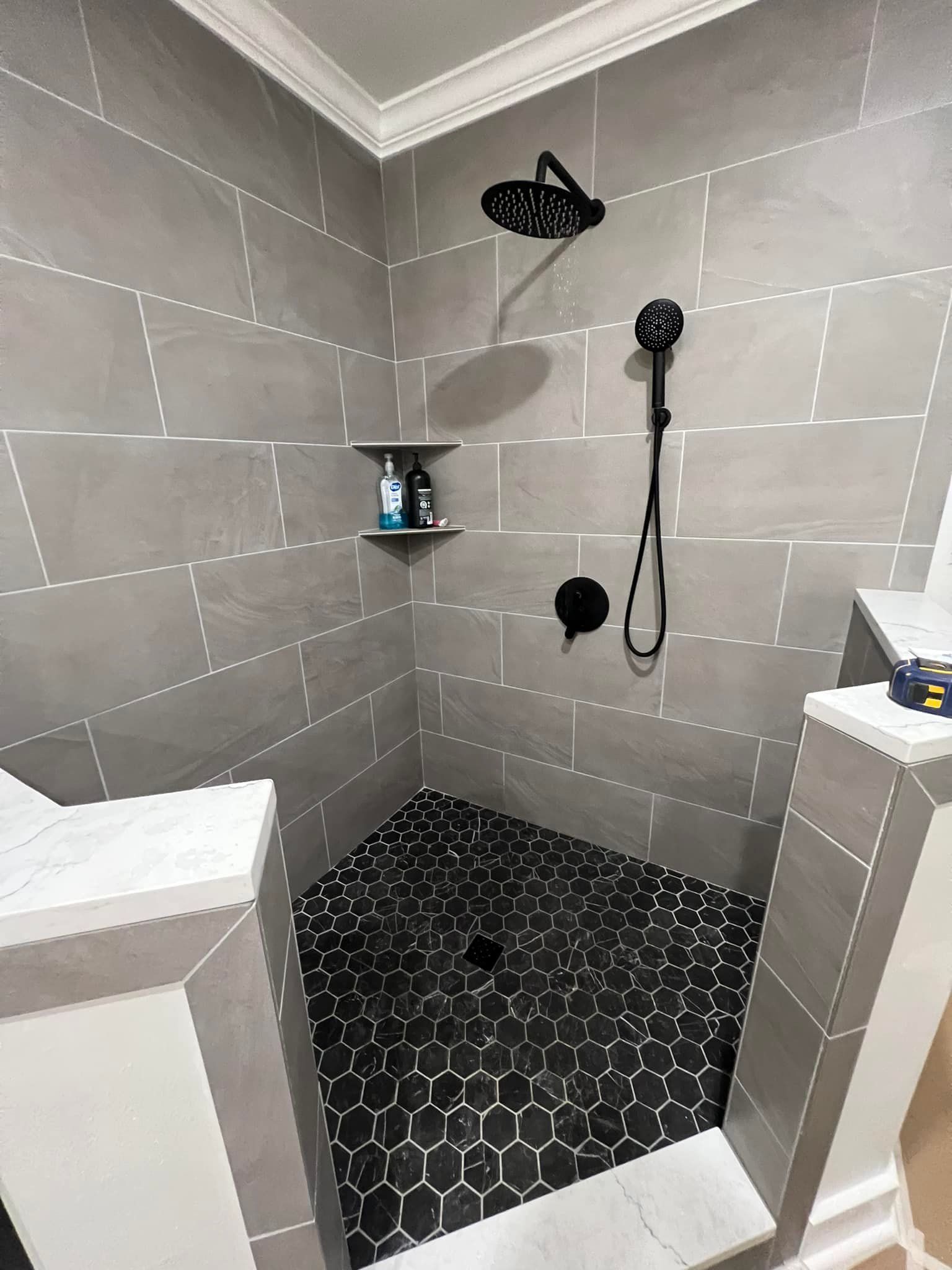 A walk in shower with black tiles and a black shower head.