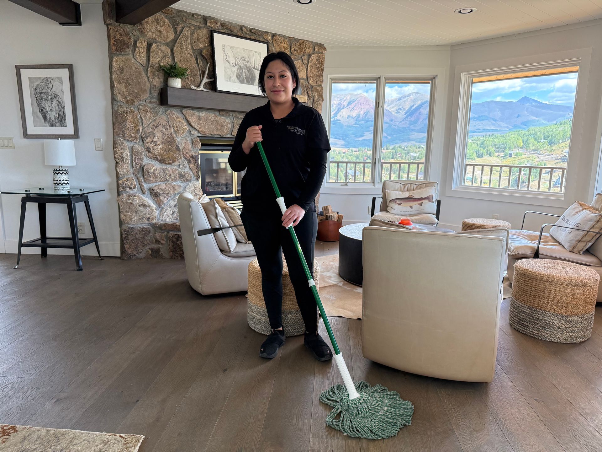 Woman vacuuming a light-colored rug in a living room. She wears jeans and a gray shirt.