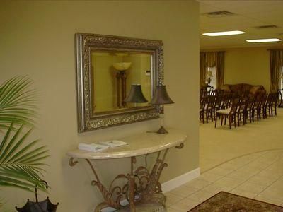 Lobby hallway with ornate mirror, table lamp, and chairs in a warmly lit room.