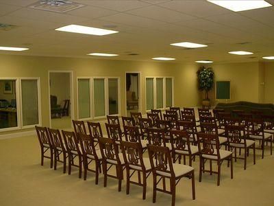 Empty banquet hall with rows of chairs, beige carpet, and fluorescent ceiling lights