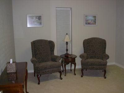 Living room with two upholstered armchairs, small table with lamp, and framed wall art.