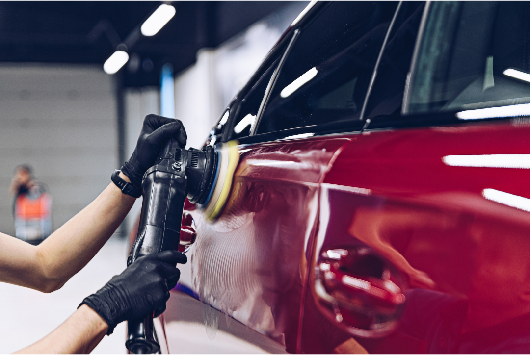 A person is polishing a red car with a machine.