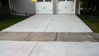 Concrete driveway leading to two white garage doors beside a lawn and sidewalk.
