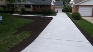 Fresh concrete driveway leading to a suburban house and garage, bordered by dark mulch and green lawn.