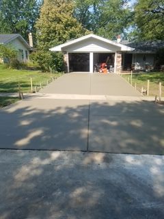 Concrete driveway leading to a single-car garage with a white gable roof and trees in the yard