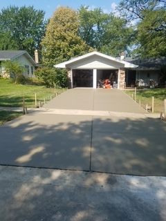 Residential driveway with a steep concrete ramp leading to a white garage under a partly open carport.