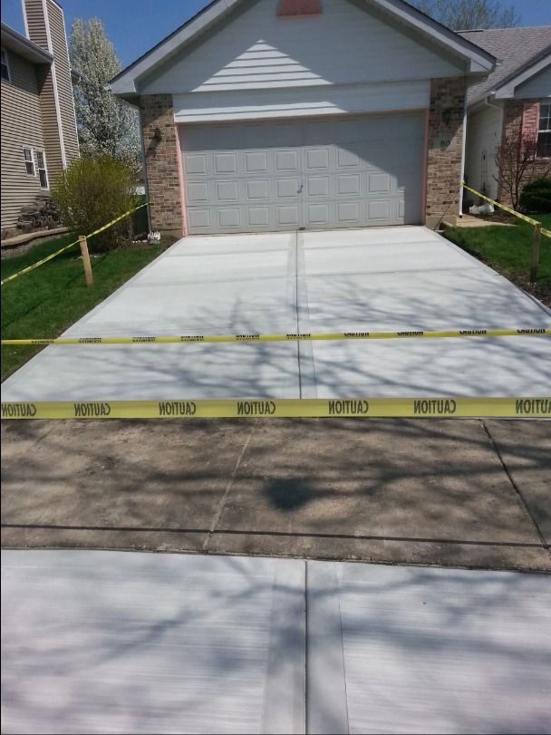New concrete driveway with caution tape in front of a house with a garage door and green lawn.