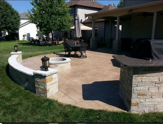 Outdoor patio with fire pit, seating, and built-in grill area, surrounded by a low wall.