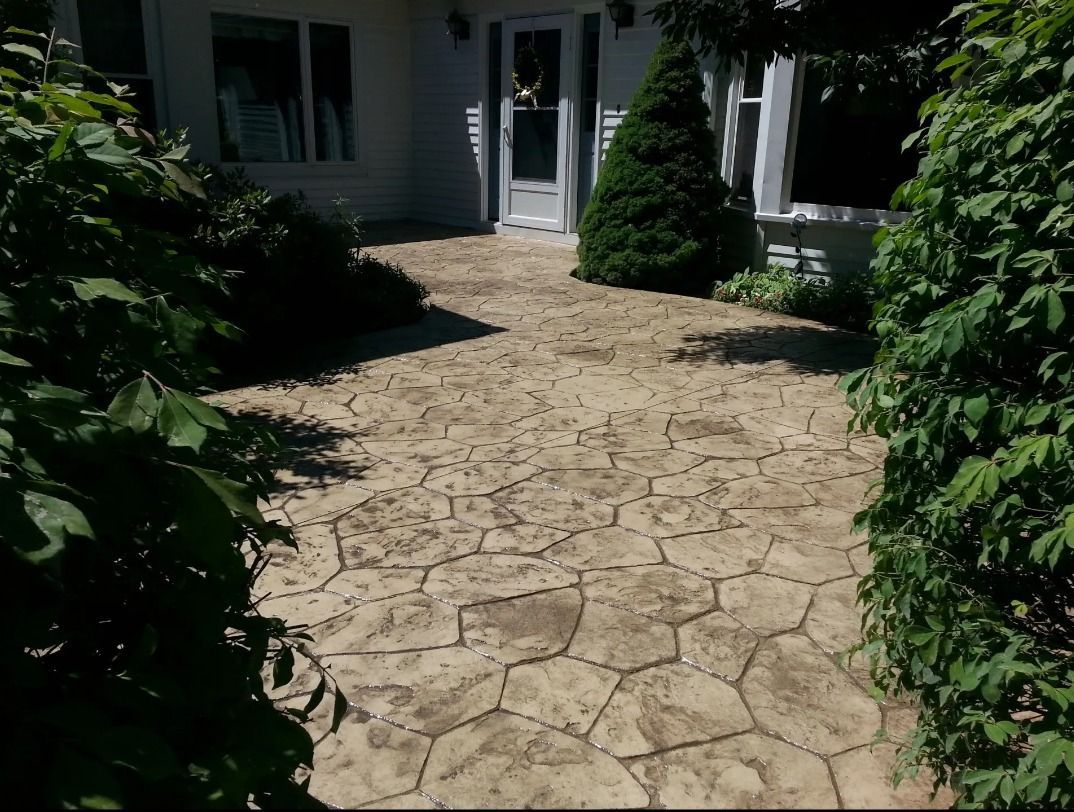 Stamped concrete patio leading to a white house entrance, flanked by green bushes.