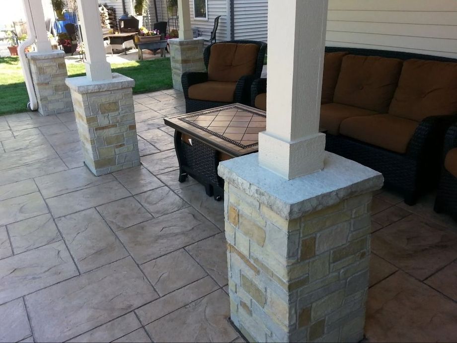 Beige stone patio with columns, outdoor seating, and a fire table.