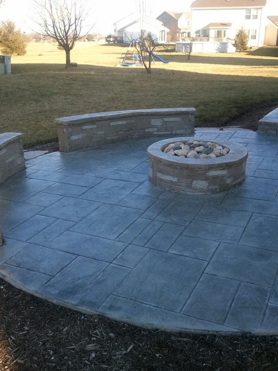 Stone patio with built-in fire pit, surrounded by low walls, in a backyard.