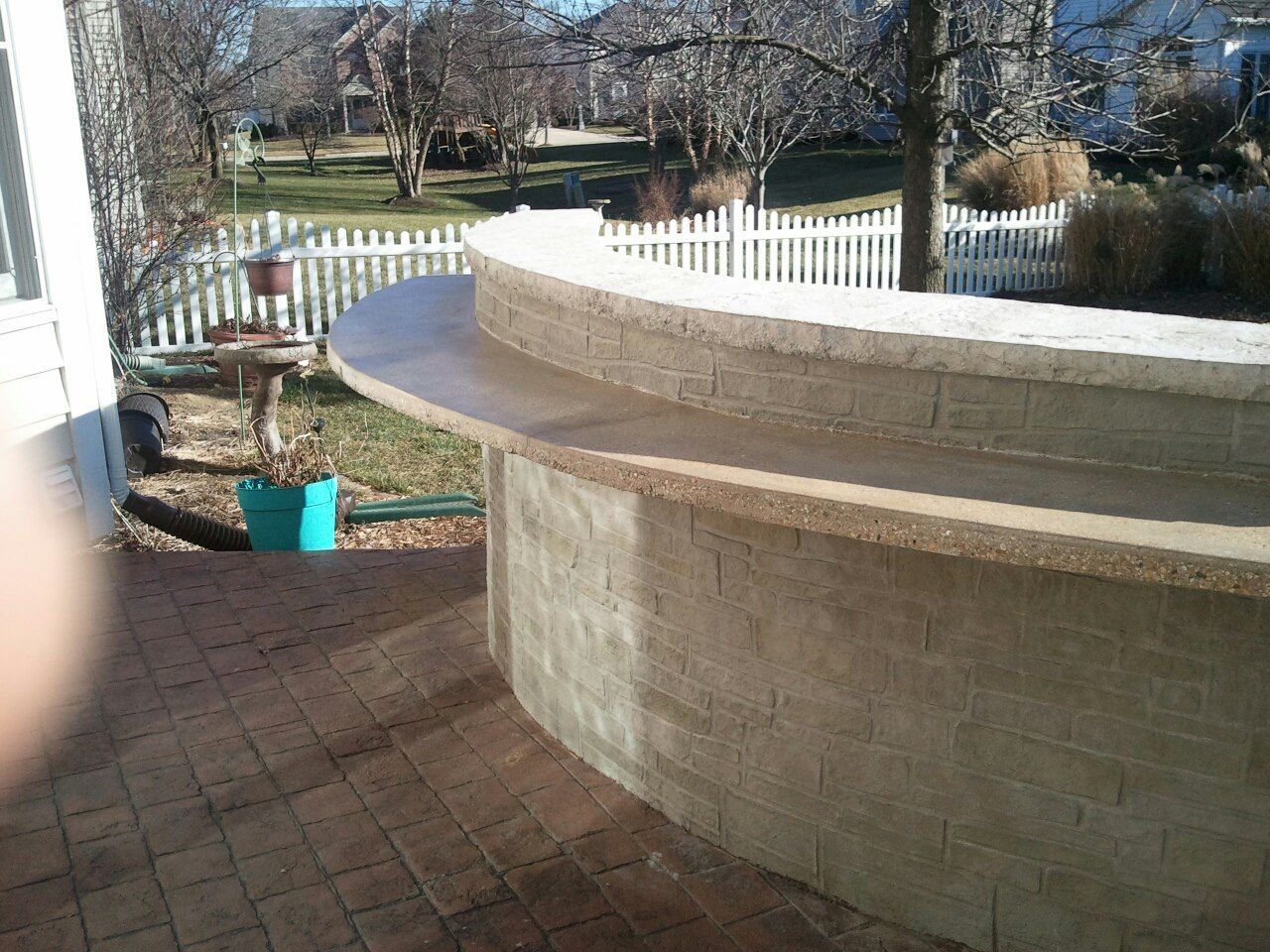 Outdoor curved bar made of stone and concrete, on a brick patio.