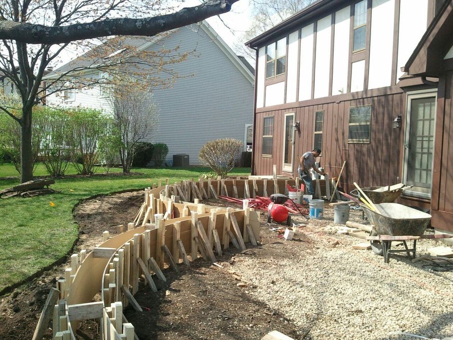 Construction of a curved concrete structure in a yard, with forms in place and a worker present.