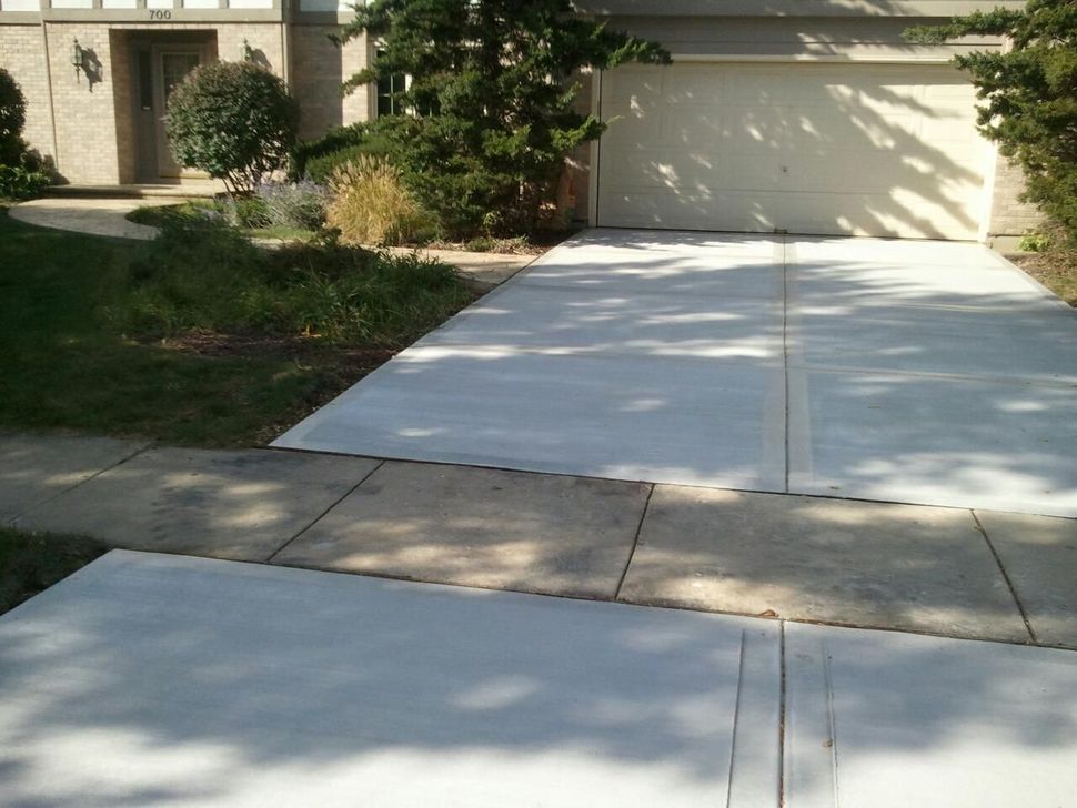 Concrete driveway and sidewalk leading to a garage. Overcast, grassy yard.