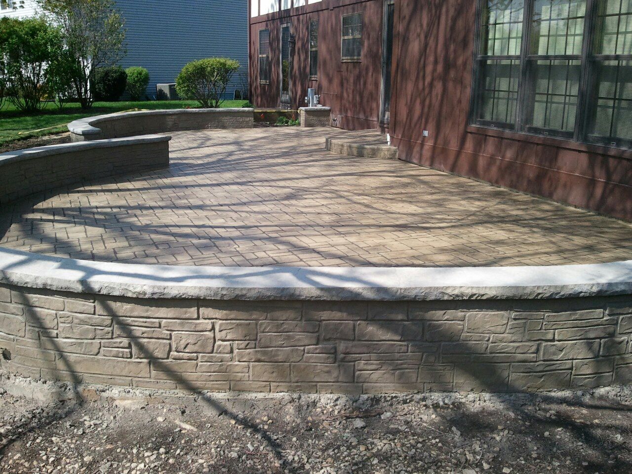 Concrete patio with brick textured retaining wall and steps, next to a red brick building.
