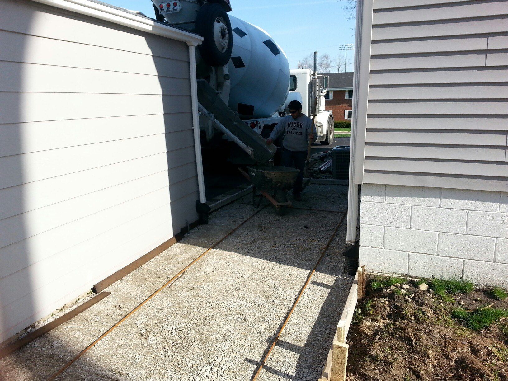 Concrete truck pouring concrete into driveway; worker with wheelbarrow.