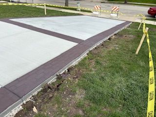 Fresh concrete sidewalk panels beside grass and caution tape along a roadside repair area