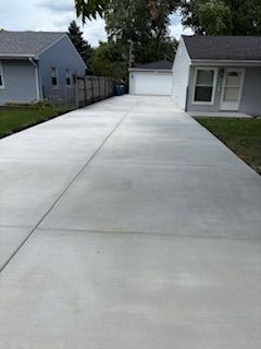 Wide concrete driveway leading to a white garage between two houses on a cloudy day