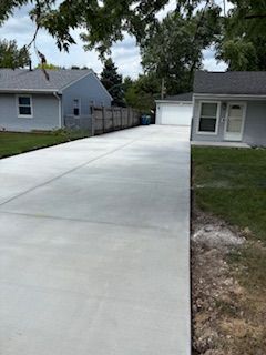 Fresh concrete driveway leading to a garage beside a gray house in a suburban yard