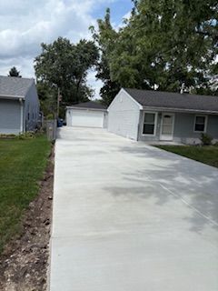 Freshly poured concrete driveway between two gray houses, leading to a detached garage.