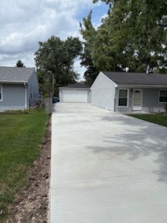 Fresh concrete driveway leading to a white garage beside a gray house under a cloudy sky