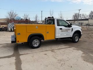 Yellow utility truck parked on pavement, side view, with white cab and equipment compartments.